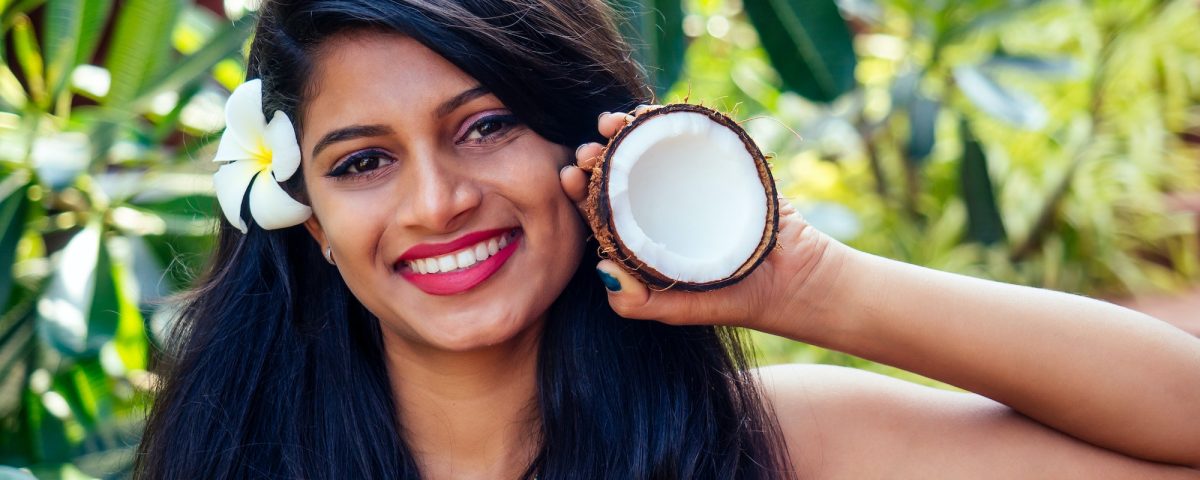 indian woman applying coconut oil dark brunette long hair in a hand on green summer